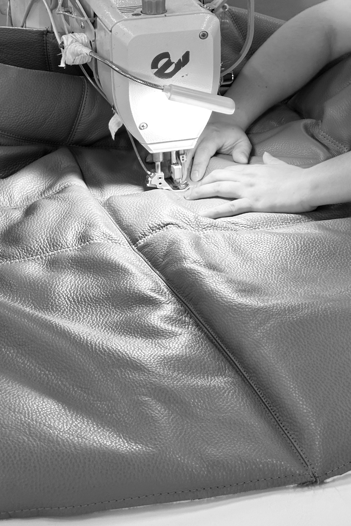Close detail of hands guiding leather through a stitching machine
